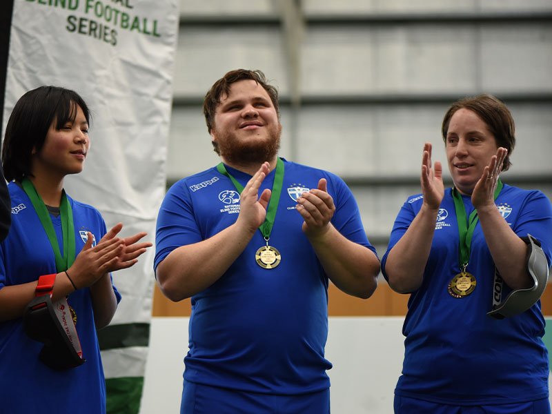 Photo of South Melbourne FC blind footballers Bo, Nathan and Shae applauding during the National Blind Football Series medal presentation
