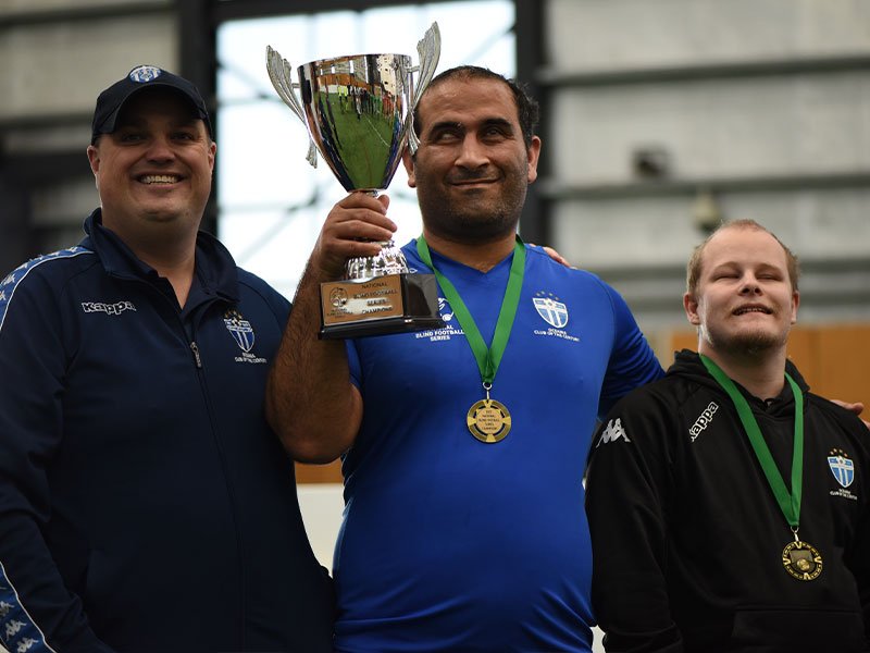 South Melbourne FC Team Manager Skip Fulton with blind footballers Amir Abdi and Brand Pinkett holding the trophy for winning the National Blind Football Series